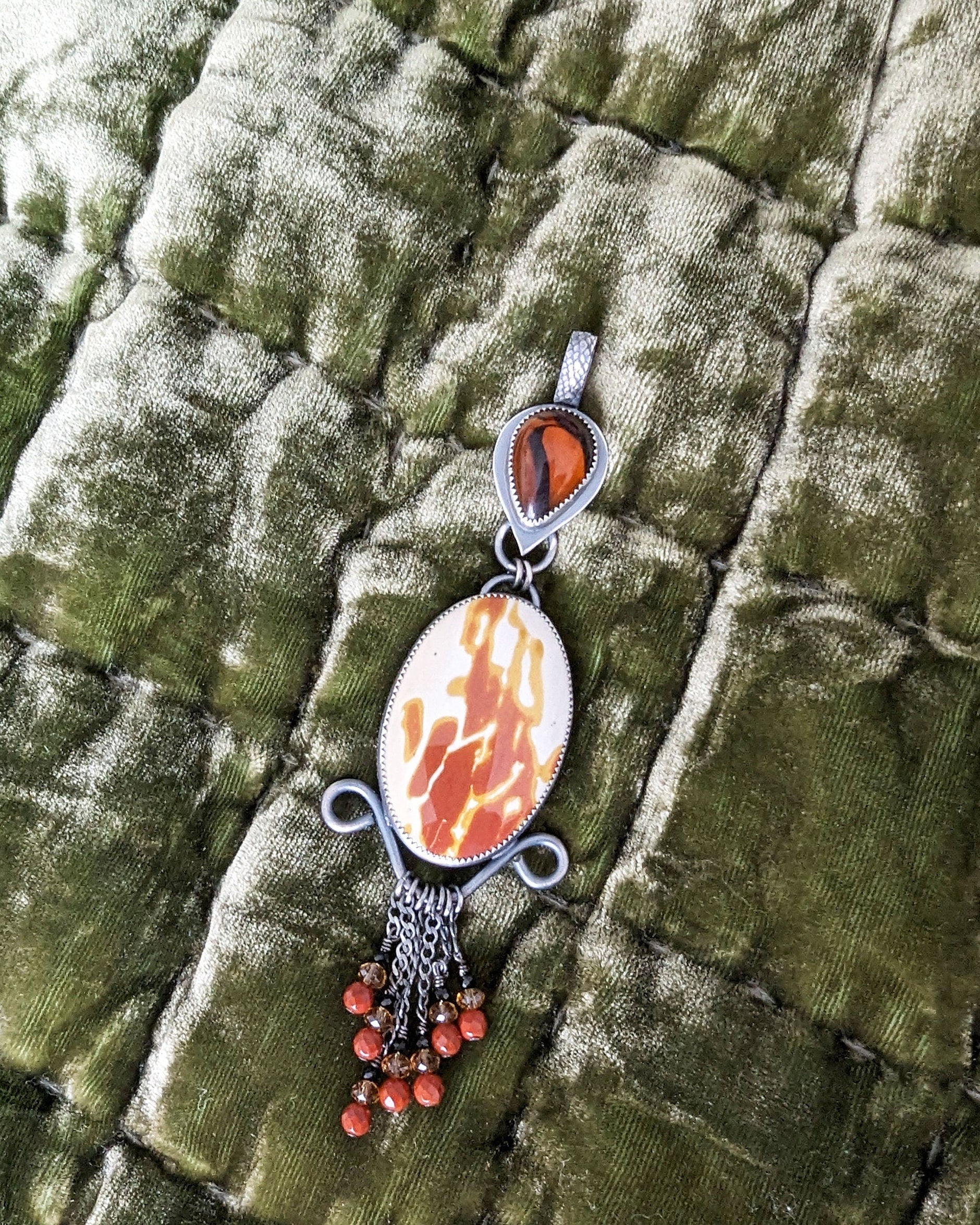 Jewelry pendant with a stone and beads on a textured green fabric background