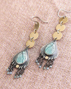 Pair of earrings with turquoise stones and gold accents on a textured beige surface.