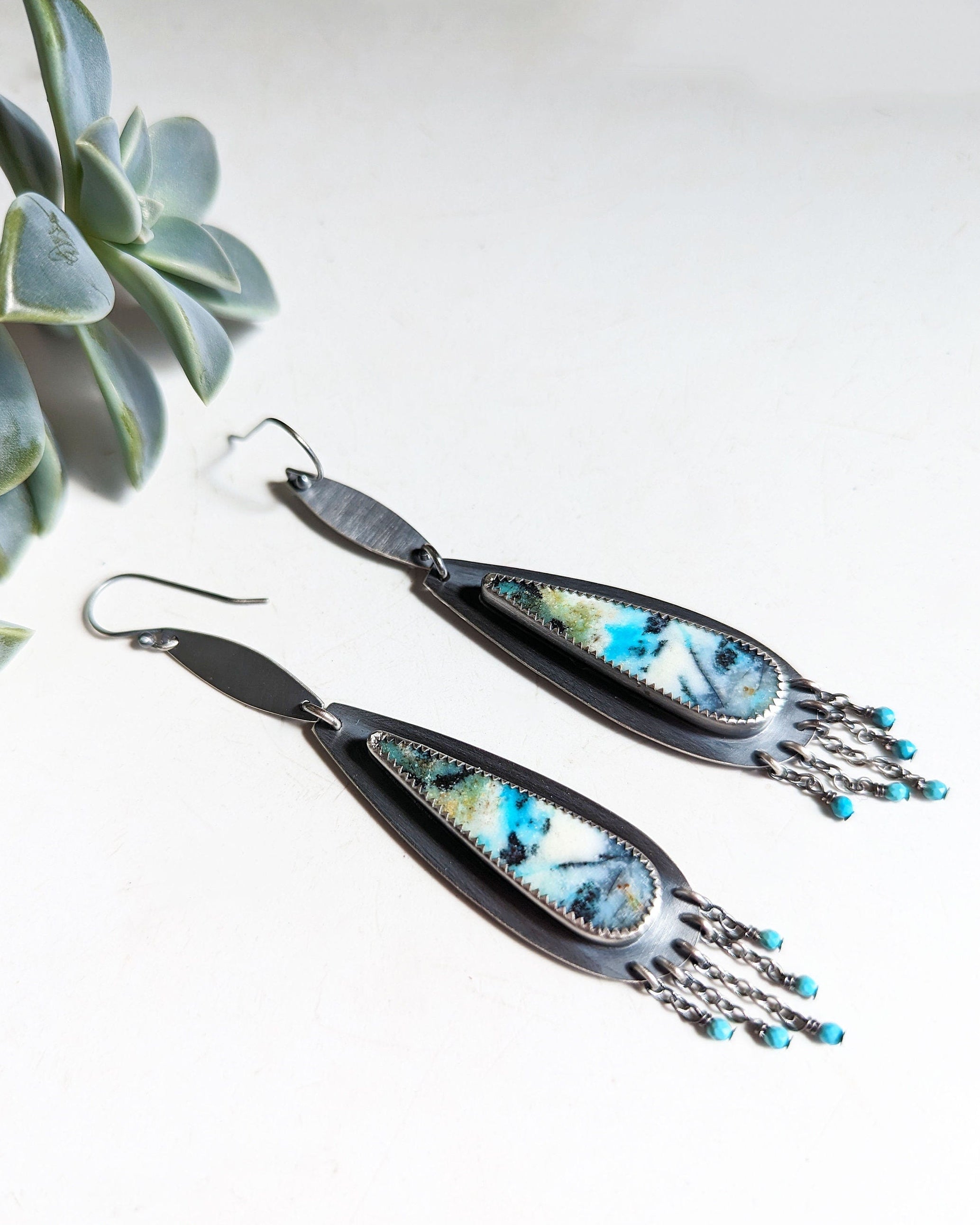 Pair of earrings with blue accents on a white background, featuring a plant.