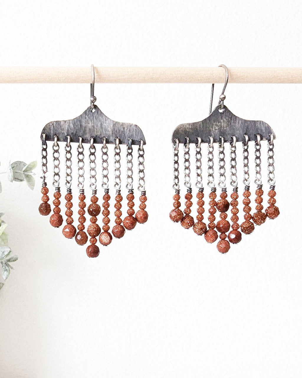 Close-up of hand-hammered oxidized sterling silver earrings with goldstone beads hanging
