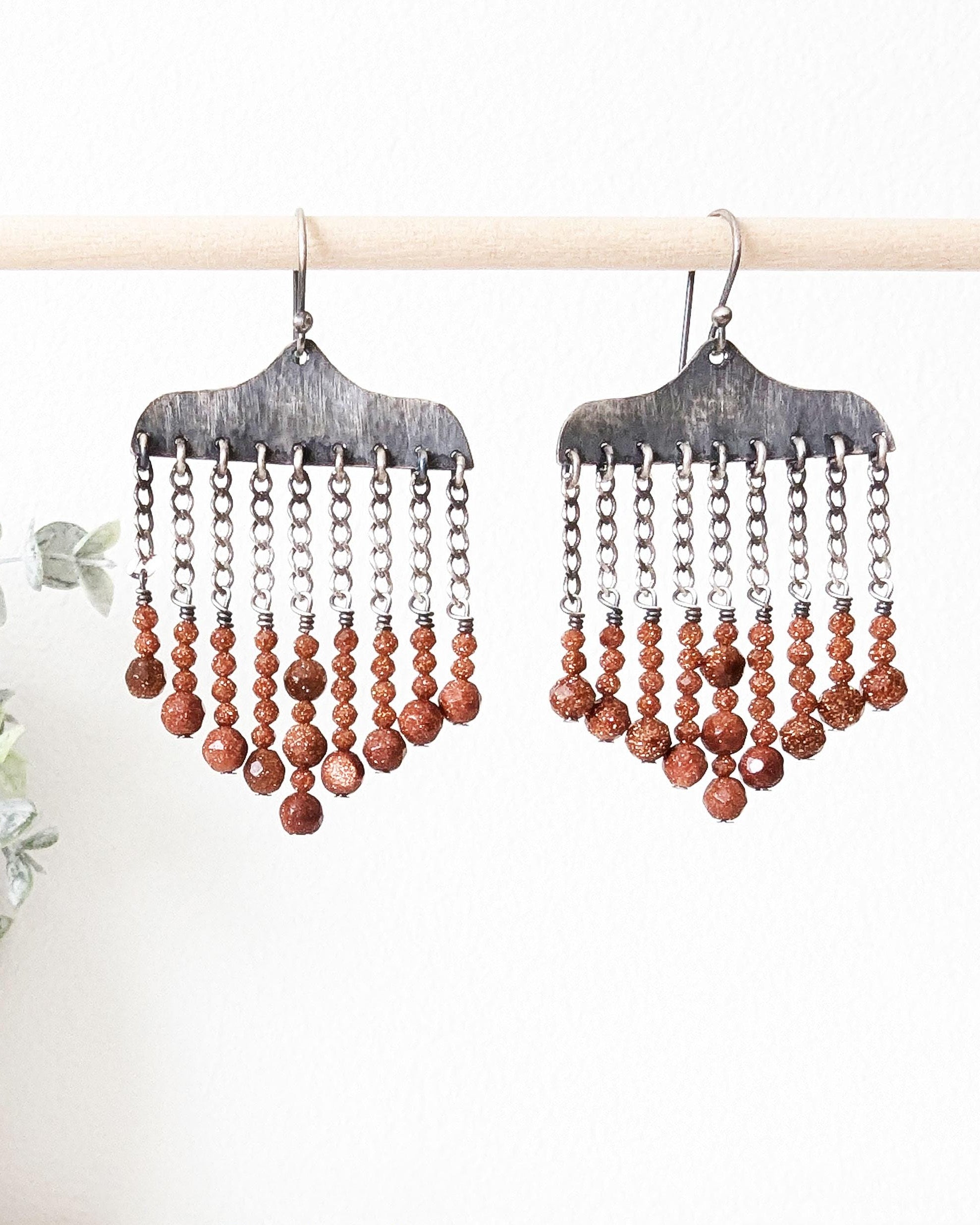 Close-up of hand-hammered oxidized sterling silver earrings with goldstone beads hanging
