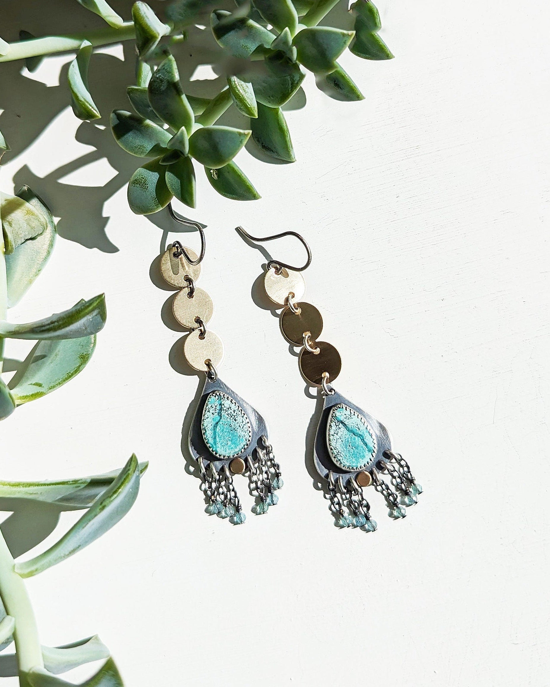 Pair of earrings with turquoise stones hanging on a plant
