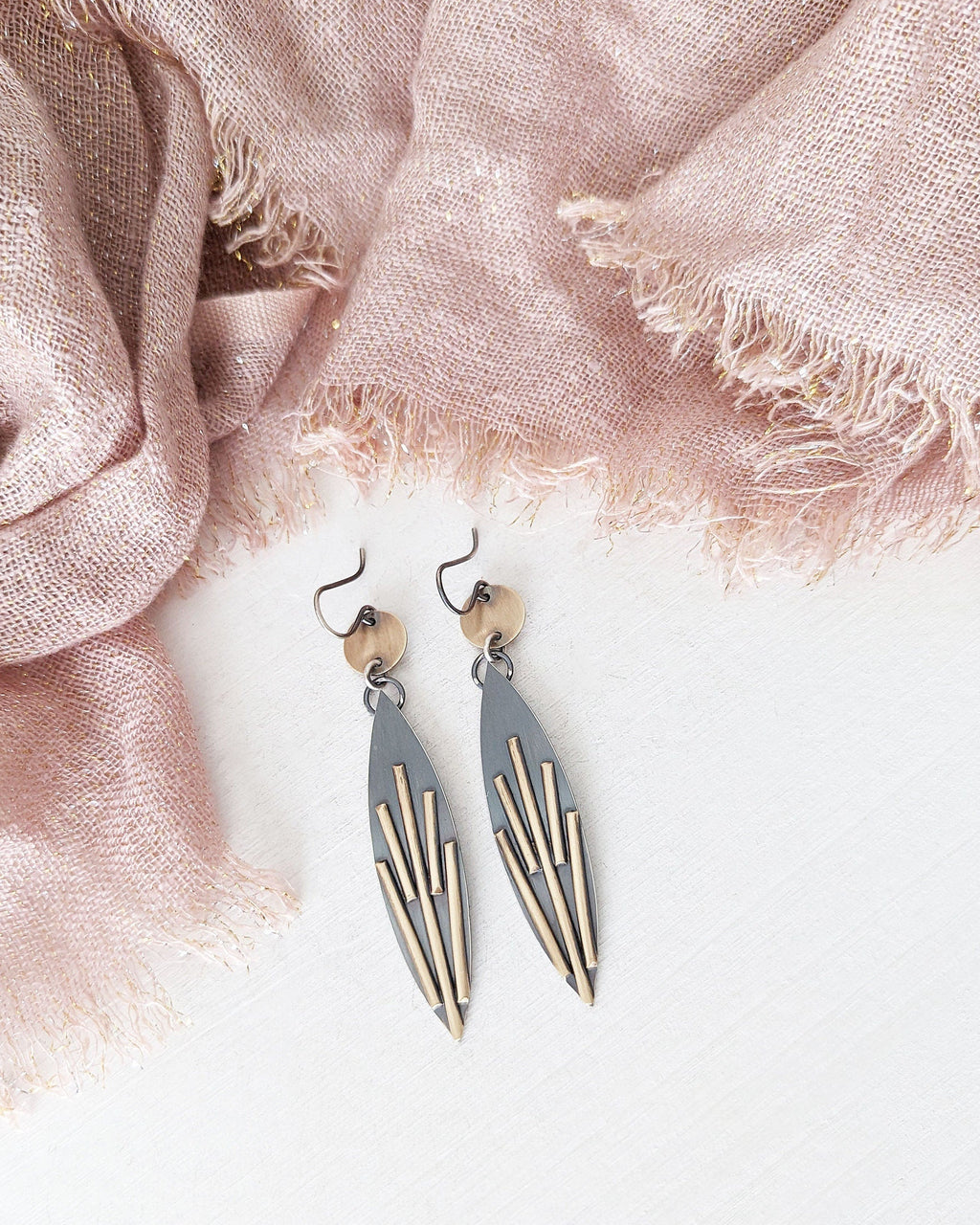 Pair of earrings on a light pink fabric background.