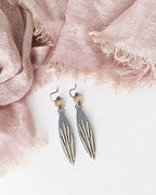 Pair of earrings on a light pink fabric background.