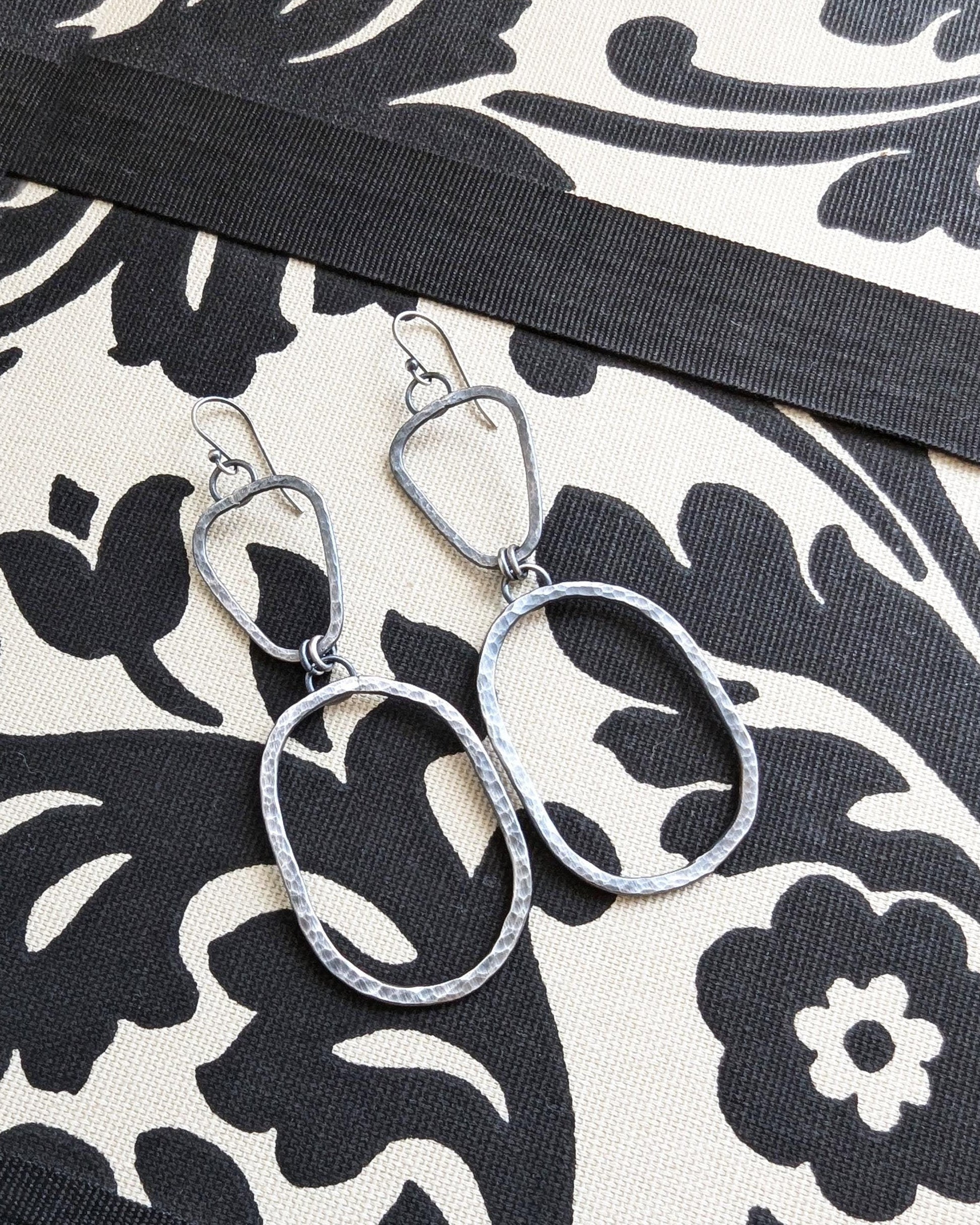 Silver earrings on a black and white patterned fabric.