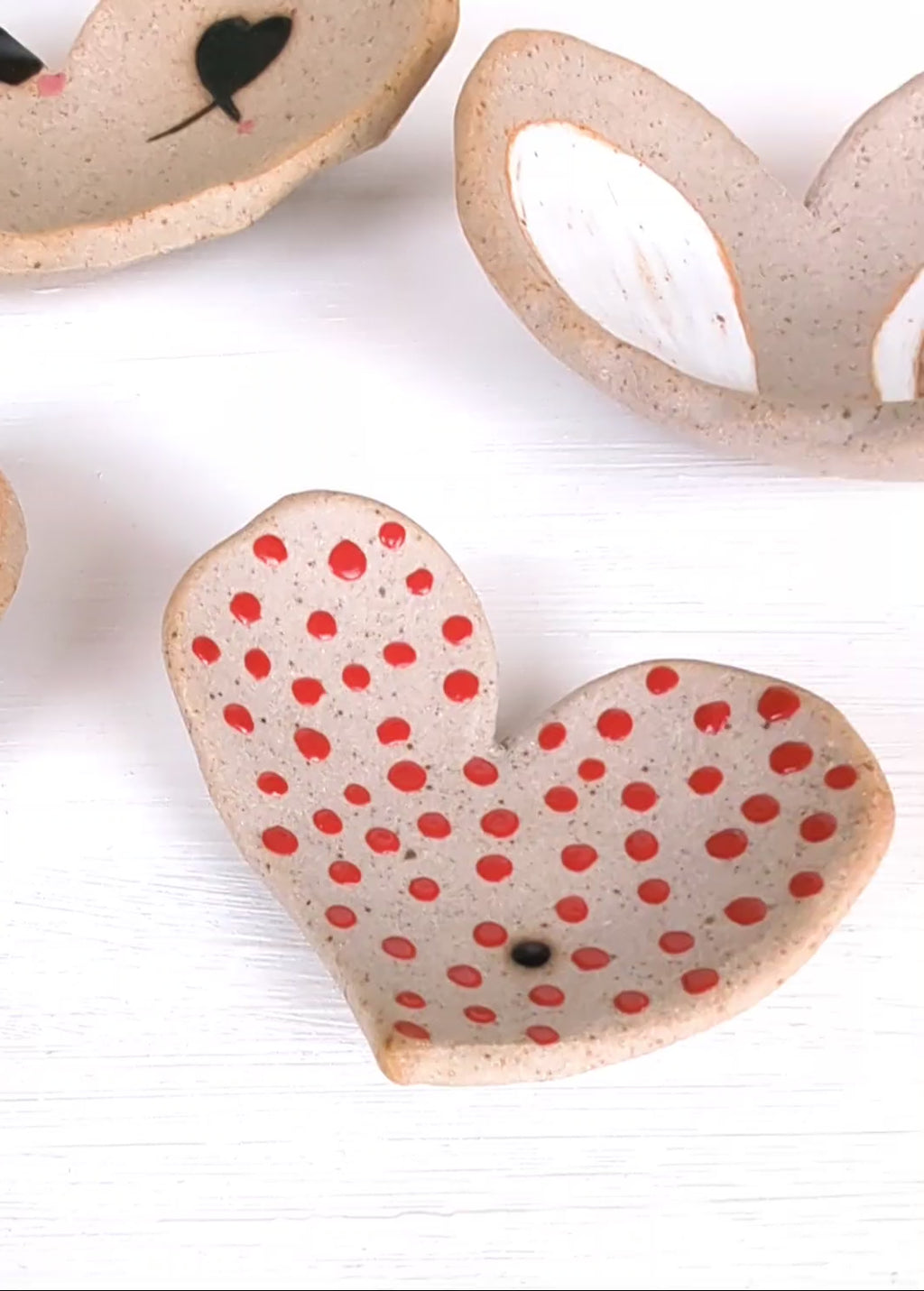 Video of 4 organic heart stoneware nesting dishes with unique glazed deigns with spots and hand painted graphic designs and raw stonware areas.
